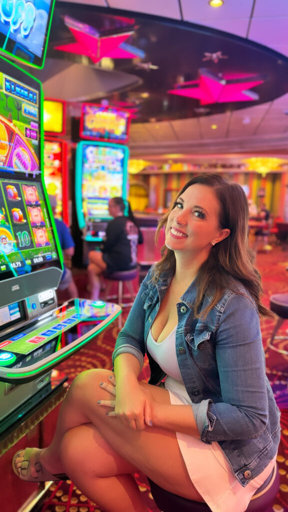 A woman poses in front of a cruise ship casino slot machine.