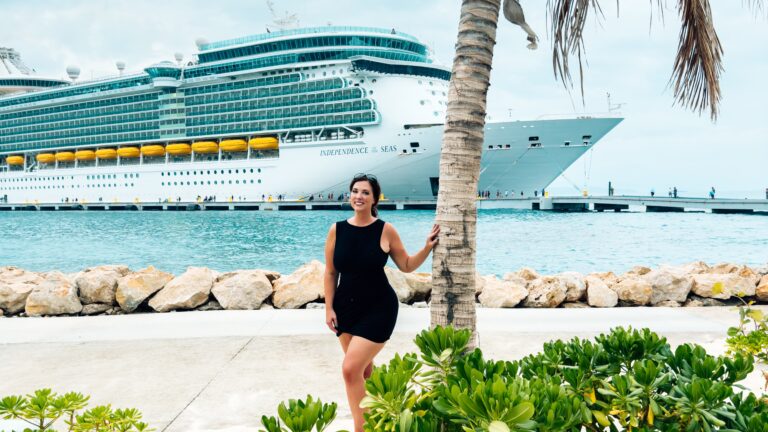 A woman standing by a palm tree with a Royal Caribbean cruise ship docked behind her in Labadee, Haiti