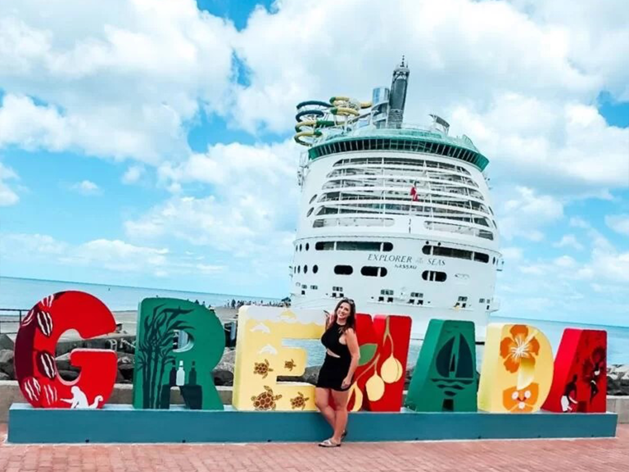 Professor Melissa posing in front of a colorful "Grenada" sign at the St. George cruise port with Royal Carribean's Explorer of the Seas