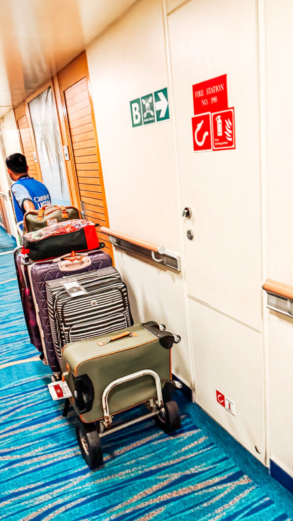 A cruise line staff member hauls luggage down a cruise ship hallway to deliver to passengers