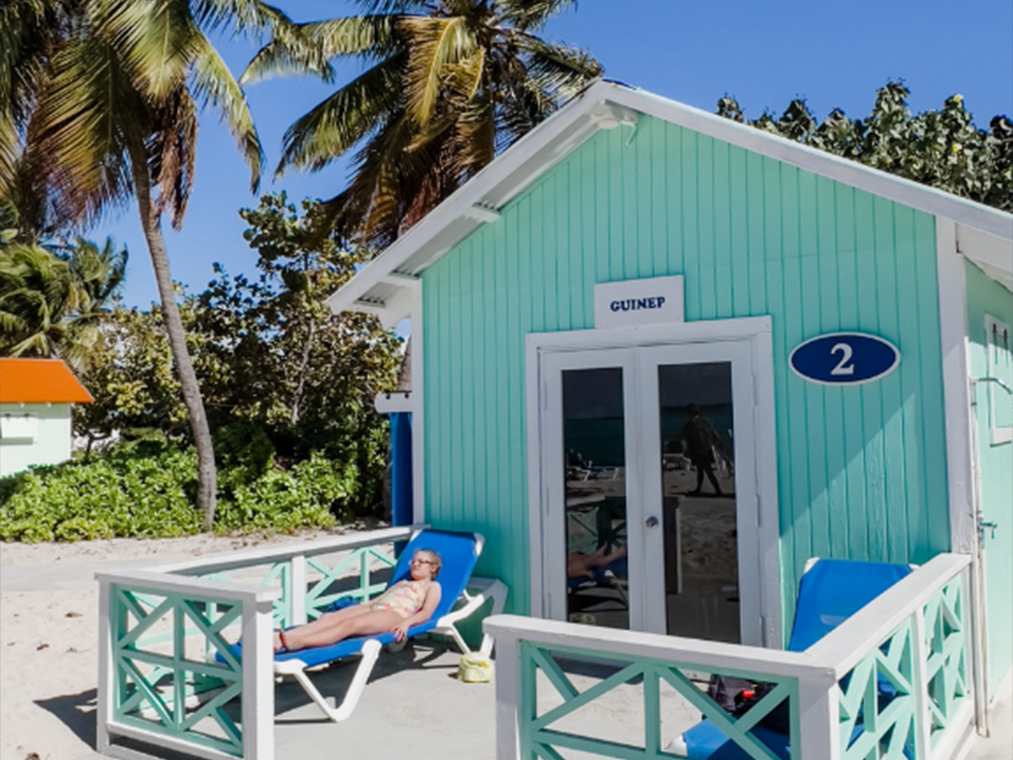 A light blue beach cabana with a sign that reads "GUINEP 2" stands against a clear blue sky.