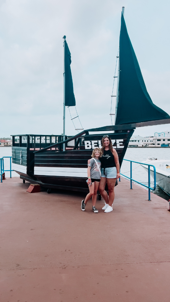 Two women stand together on a dock in front of a black and white boat with "BELIZE" written on its side.