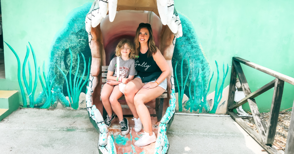 Two women are sitting inside a decorative giant shell, which is part of a colorful, ocean-themed display.