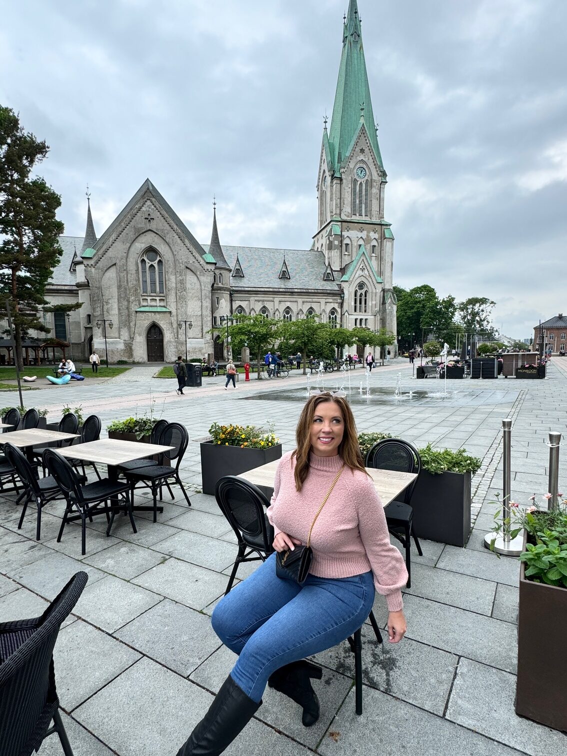 A woman poses in a cafe chair in front of the Kristiansand Cathedral in Norway. 
