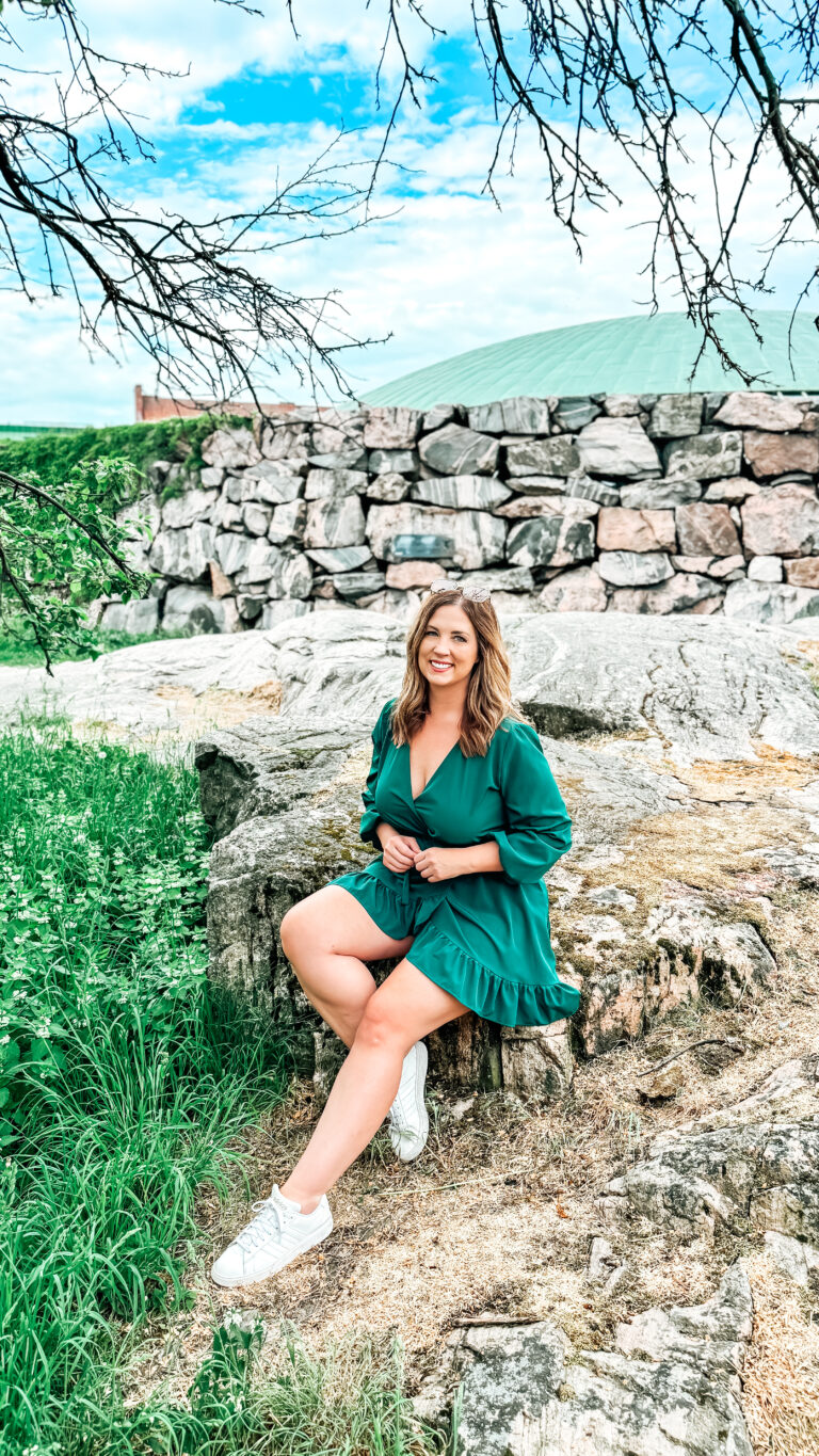 Smiling woman in a green dress sitting on a rock in a park