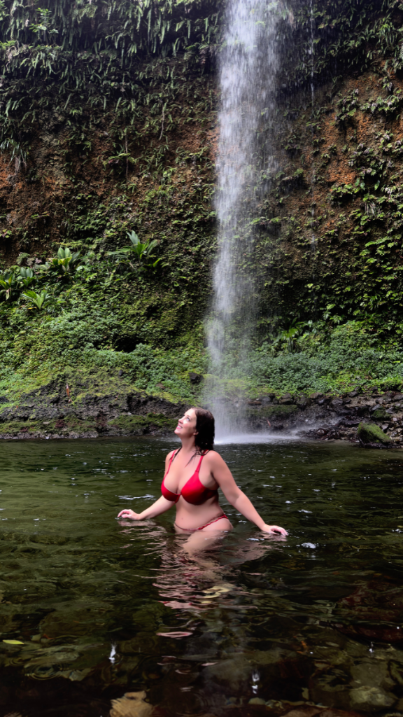 A woman in a red bikini enjoys the refreshing waters of a natural pool beneath a cascading waterfall.
