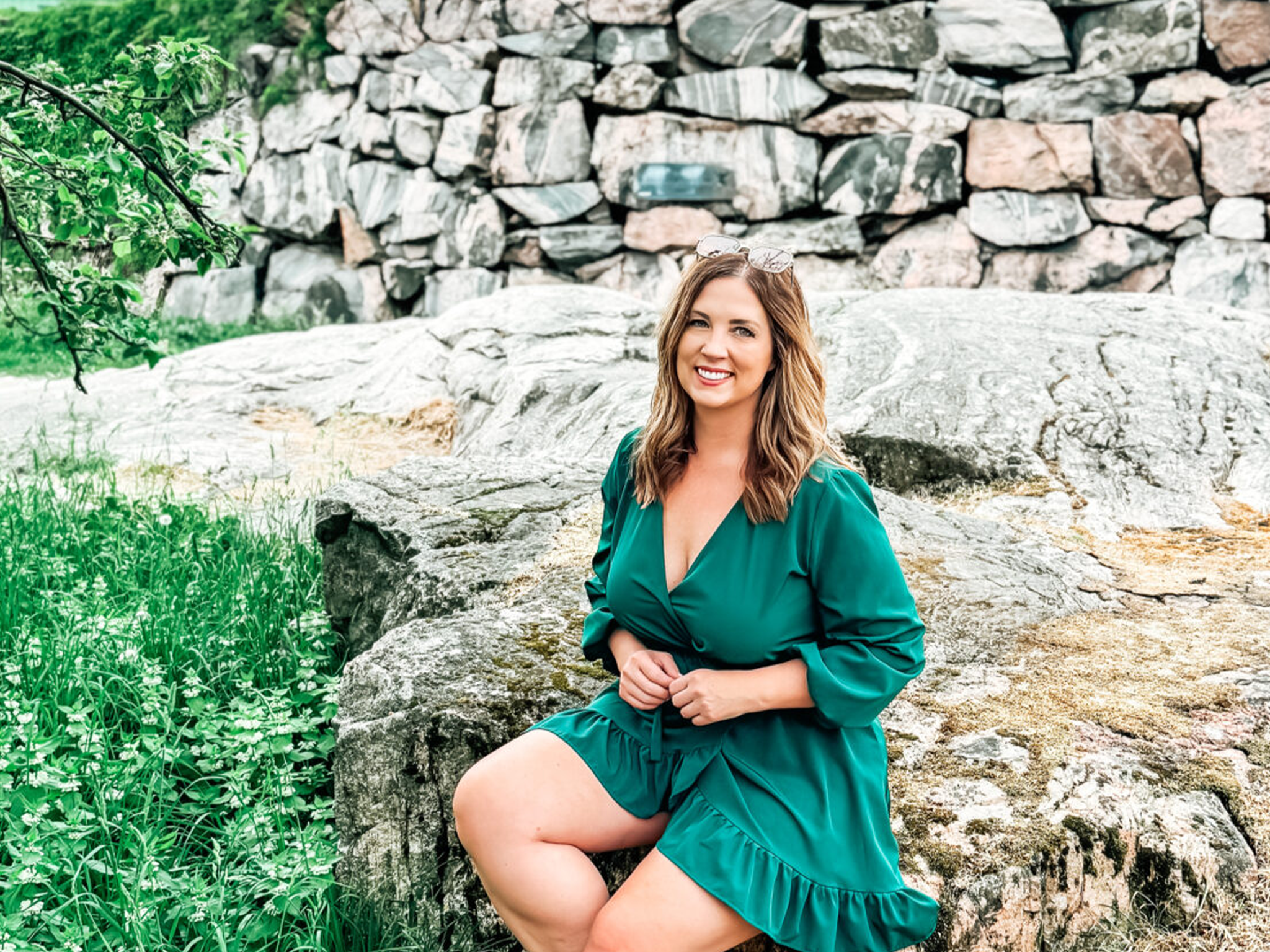 Smiling woman in a green dress sitting on a rock in a park