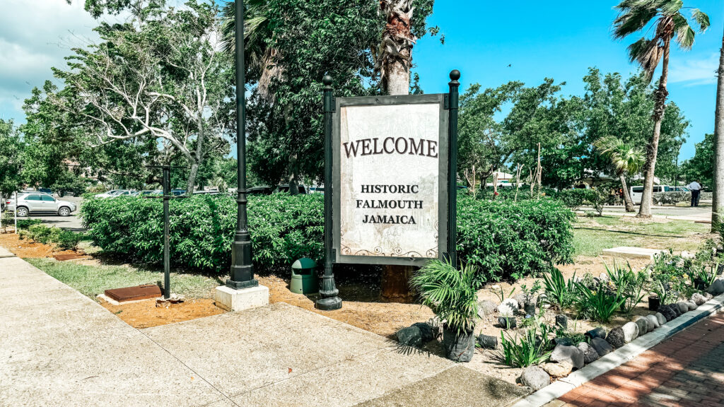  A welcome sign for Historic Falmouth, Jamaica, surrounded by greenery and trees.