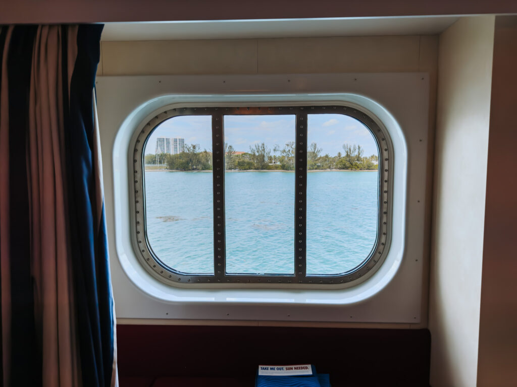 A view of the ocean from a cruise ship stateroom window, with a glimpse of the shoreline and buildings in the distance