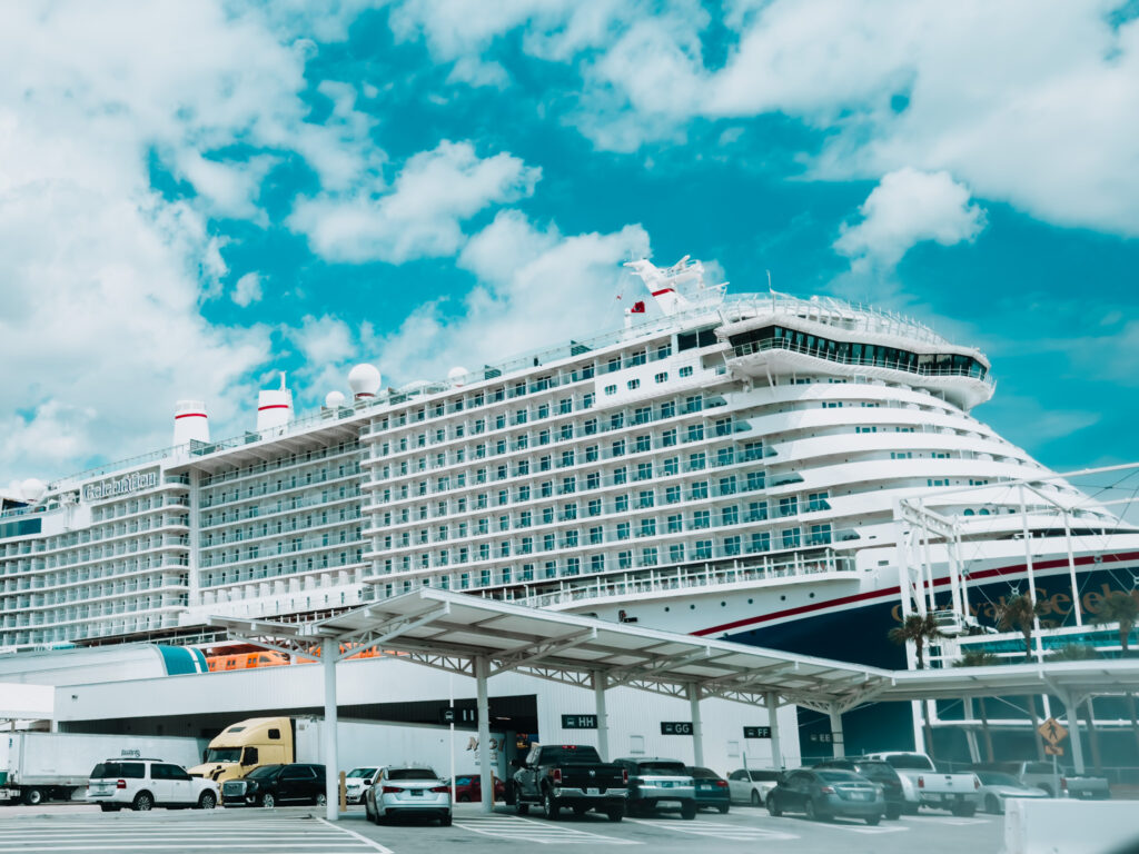 A large cruise ship docked at the port, with a bright blue sky and a few clouds overhead.